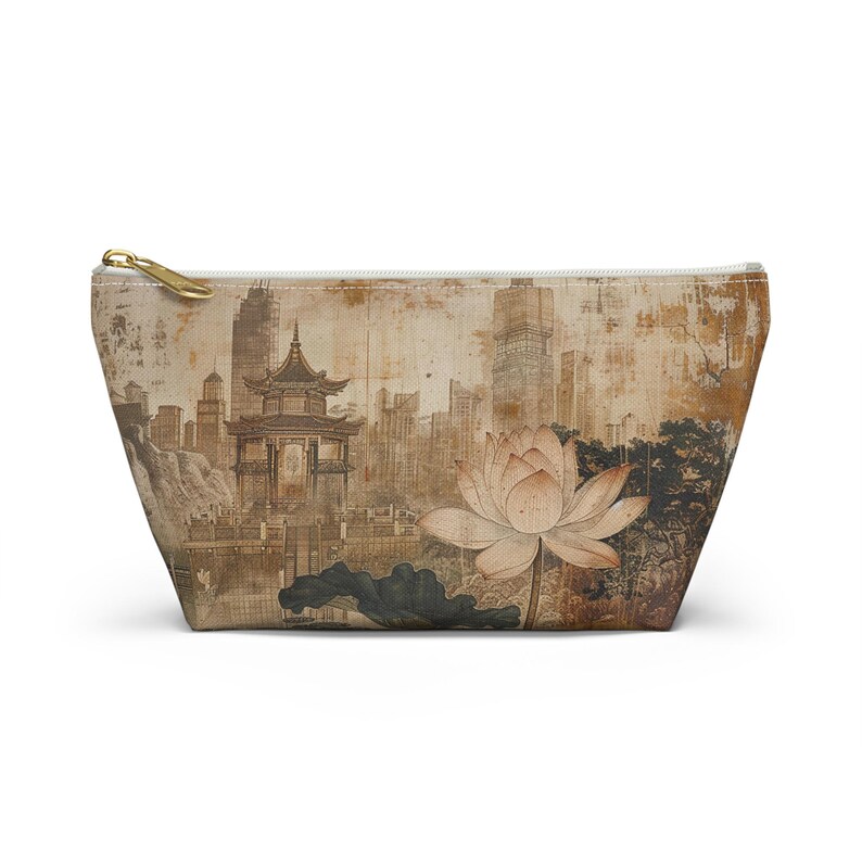 May include: A beige zippered pouch featuring an Asian-inspired design. The artwork depicts a pagoda, a lotus flower, and a cityscape in shades of brown and beige. The pouch has a gold-colored zipper.