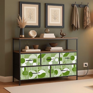 May include: A contemporary console table in black metal and wood, featuring drawers with a green and white geometric design. The table includes a shelf with decorative items such as framed art, vases, and books. The wall is painted dark green.