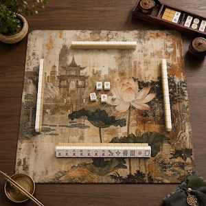 May include: A square mahjong mat featuring a printed landscape with a traditional pavilion, a large lotus flower, and dark green lily pads. The mat is arranged with white mahjong tiles in rows and columns, alongside a wooden tile rack and dice.