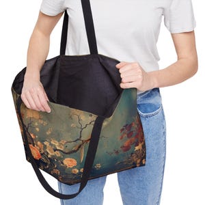 May include: A large tote bag with a floral design featuring peach and yellow flowers, branches, and leaves against a teal background. The bag has black straps and a black interior. The bag is being held open.