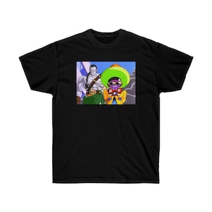 Può includere: T-shirt nera con una grafica colorata di due personaggi anime. Un personaggio indossa una giacca gialla e occhiali da sole, l'altro è una figura muscolosa con una spada. La grafica include le lettere "R R".