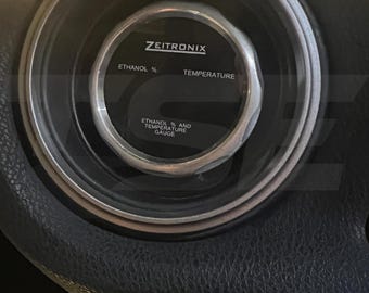 May include: A circular Zeitronix gauge with a silver bezel and a black face. The display features the text Zeitronix, Ethanol %, Temperature, and Ethanol % and Temperature Gauge printed in white lettering against the dark background.