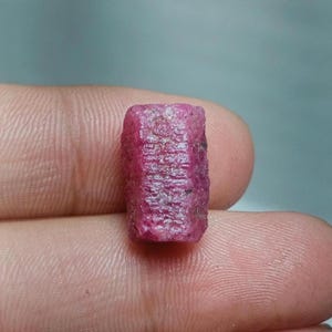 Op de afbeelding: Een close-up van een diep roze, gefacetteerde robijn edelsteen. De robijn heeft een rechthoekige vorm en een glad, gepolijst oppervlak.