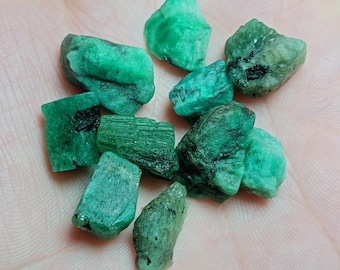 May include: A collection of rough, green emerald gemstones. The emeralds are various sizes and shapes, with some showing natural inclusions.
