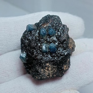 May include: A dark gray rock with several small, blue, faceted crystals embedded in it.