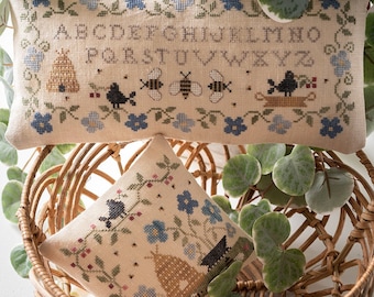 Puede incluir: Dos fundas de cojín bordadas con un tema de abejas y pájaros. La almohada más grande presenta el alfabeto en una fuente vintage y una colmena. La almohada más pequeña presenta una colmena, pájaros y flores.