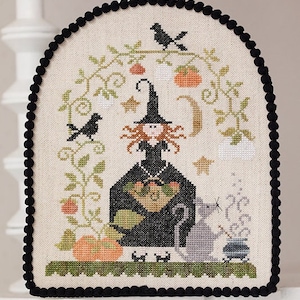 May include: A cross-stitch pattern featuring a witch with a black hat and red hair, holding a basket of pumpkins. A black cat sits next to her, and a cauldron with smoke is in the background. The design is surrounded by vines, pumpkins, and stars.