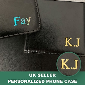 Puede incluir: Dos fundas de teléfono de cuero negro con nombres personalizados. La funda superior tiene el nombre "Fay" en colores arcoíris. La funda inferior tiene el nombre "K.J." en letras doradas.