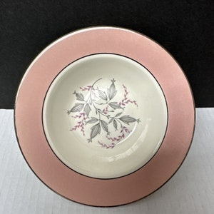 May include: A white ceramic bowl with a pink rim and a floral design. The bowl has a gold trim around the rim.
