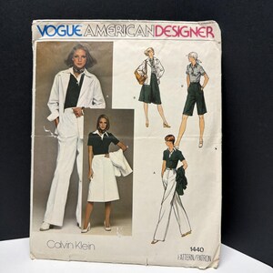 May include: A Vogue American Designer sewing pattern envelope for Calvin Klein design 1440. The front features illustrations and photographs of a polo shirt, a blazer, wide-leg trousers, and a skirt in white, dark green, and neutral tones.