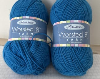 May include: Two balls of blue Worsted 8 yarn by Herrschners. Each ball is a full 8-ounce ball. The yarn is a vibrant shade of blue, and the labels feature the brand name and yarn type.