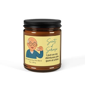 Peut inclure: Bougie en pot de verre marron avec un couvercle noir. L'étiquette présente un dessin animé d'une personne âgée tenant un dentier, avec le texte "Scents of Sarcasm". La bougie contient 255 g de cire de soja 100% naturelle.
