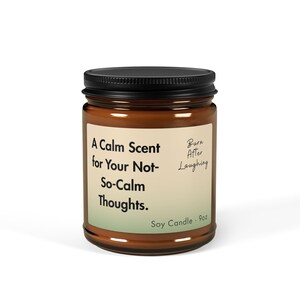 Peut inclure: Un pot en verre brun avec un couvercle noir, contenant une bougie de soja. L'étiquette indique "A Calm Scent for Your Not-So-Calm Thoughts." et "Burn After Laughing." La bougie est de 255 grammes.