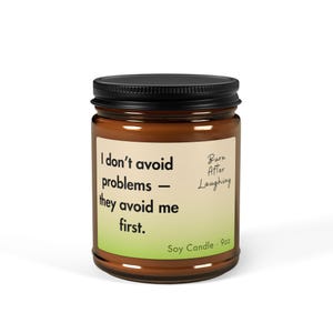 May include: A brown glass jar with a black lid, labeled "I don't avoid problems - they avoid me first." The label also reads "Burn After Laughing" and "Soy Candle - 9oz."