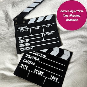 May include: Two black and white film clapperboards. The top clapperboard has the words "PROD.NO., SCENE, TAKE, ROLL, DATE, PROD.CO., DIRECTOR, CAMERAMAN, SOUND" printed on it. The bottom clapperboard has the words "PRODUCTION, DIRECTOR, CAMERA, DATE, SCENE, TAKE" printed on it.