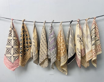 May include: Eight patterned fabric squares hang from a string. The squares are in various colors and patterns, including black, white, brown, red, and purple. The fabric is a light cream color.