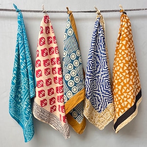 May include: Five patterned bandanas hanging from a rope. The bandanas display various designs in shades of blue, red, yellow, and white. Each bandana is folded, showcasing the different patterns and colours.