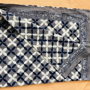 May include: A folded textile with a repeating pattern of white and navy blue four-petal flower shapes on a gray background. The border is gray with a decorative floral design. The textile is likely cotton or a similar fabric.