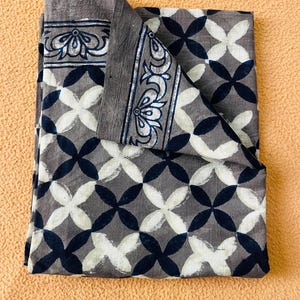 May include: Folded gray fabric with a repeating pattern of white and navy blue overlapping four-petal shapes. The border features a decorative floral design in white and navy blue.