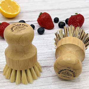 May include: Two wooden dish brushes with natural bristles. The brushes have a round wooden handle with the text "The Cotswold Eco Company" printed on the bottom.