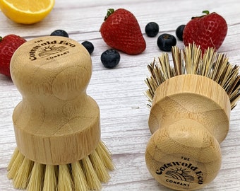 May include: Two wooden dish brushes with natural bristles. The brushes have a round wooden handle with the text "The Cotswold Eco Company" printed on the bottom.
