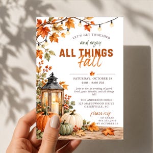 May include: A rectangular invitation card featuring autumn-themed illustrations of orange and white pumpkins, a lit lantern, and maple leaves. The text reads: Let's get together and enjoy all things fall, Saturday, October 18, 4:00-8:00 PM, The Anderson Home.