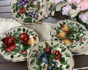 May include: Set of four ceramic dinner plates with a white background and colorful fruit designs. The plates feature grapes, apples, pears, and plums.
