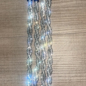 May include: A set of five silver-colored, rhinestone-encrusted keychains with blue accents. Each keychain features a silver clasp and a twisted, sparkling design. The keychains are displayed against a wooden background.