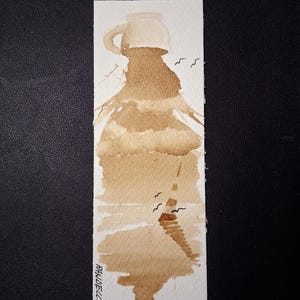 Può includere: Segnalibro ad acquerello con la silhouette di una caffettiera in tonalità marroni, che ricorda una montagna. Piccoli uccelli neri sono dipinti nel cielo. La firma e la data dell'artista, "RANDELLI 2023", sono visibili.