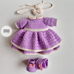 Puede incluir: Un conjunto de ropa de muñeca de ganchillo hecho a mano en tonos morados y crema. El conjunto incluye un vestido, zapatos, una diadema y puños. El vestido presenta un cuello redondo y una falda acampanada. El texto en la imagen dice "CROCHET DOLL CLOTHES PATTERN".