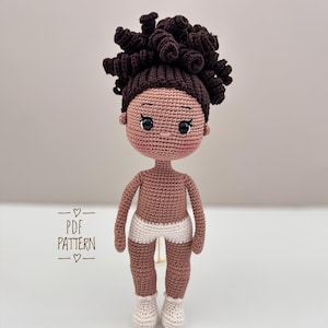 Puede incluir: Una muñeca de ganchillo hecha a mano con piel morena, cabello rizado castaño oscuro y ojos negros. La muñeca lleva pantalones cortos y calcetines blancos. La imagen incluye el texto "PDF PATTERN".