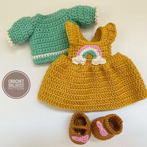 Op de afbeelding: Handgemaakte gehaakte poppenoutfitset. De set bevat een mosterdgele jurk met een regenboog, een zeegroene trui en bruine schoenen met roze details. De tekst "CROCHET DOLL OUTFIT PATTERN" staat in een cirkel.