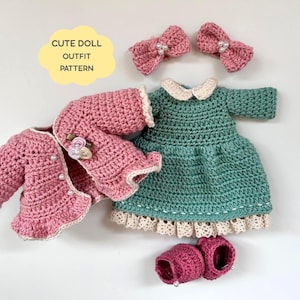 May include: A crochet doll outfit set including a dusty pink cardigan with pearl accents and floral embellishments, a teal dress with a white collar and lace trim, two pink hair bows with pearls, and a pair of pink shoes. Text reads CUTE DOLL OUTFIT PATTERN.