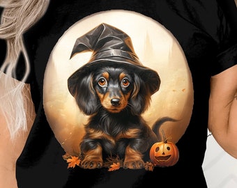 May include: Black t-shirt with a graphic of a dachshund wearing a witch's hat and holding a jack-o'-lantern. The dachshund is in front of a full moon.