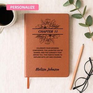 Pode incluir: Um diário de couro castanho com o texto "CAPÍTULO 11" e um design floral. O diário inclui o texto "CELEBRE A SUA CONFIANÇA CRESCENTE..." e o nome "Melissa Johnson". Um retângulo rosa com a palavra "PERSONALIZAR" está no canto superior esquerdo.