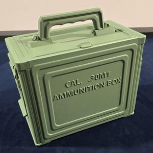 May include: A pale green ammunition box with a handle. The box is rectangular and features the embossed text "CAL .30M1 AMMUNITION BOX". It has a hinged lid and a latch. The box is designed for storage.