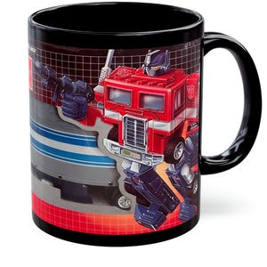 Può includere: Tazza in ceramica nera con un'illustrazione rossa, bianca e blu di Optimus Prime di Transformers. La tazza ha un manico e un bordo neri, con l'immagine del personaggio che avvolge la tazza.