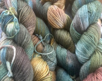 May include: A collection of yarn skeins in shades of green, brown, and beige. The yarn is arranged in a loose pile, with the ends of the skeins visible.