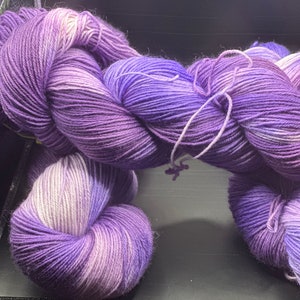 Könnte beinhalten: Lila und weißes Garnknäuel mit einem Farbverlaufseffekt. Das Garn ist weich und flauschig, perfekt zum Stricken oder Häkeln.