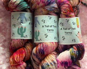 May include: Three skeins of hand-dyed yarn in a pink, purple, and blue colorway with a white base. The yarn is labeled "A Tail of Two Yarns" and "Valdosta, GA".
