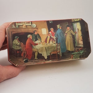 May include: A vintage tin box with a colorful illustration of a group of men in a room, one of whom is leaving through a doorway. The text "The Traveller" is printed on the bottom of the box.