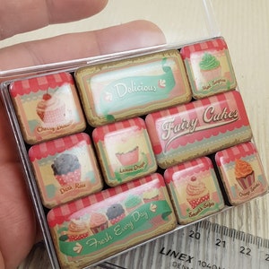 May include: A clear plastic case containing nine rectangular cupcake-themed stickers. Each sticker features a different cupcake design with text such as "Cherry Blossom", "Delicious", and "Fairy Cakes". The stickers are in a vintage style.