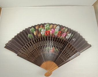 Puede incluir: Un abanico plegable marrón con un diseño floral con flores rosas, rojas, amarillas y verdes. El abanico está hecho de papel y tiene un mango de madera.