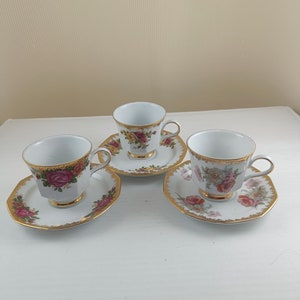 May include: Three white porcelain teacups with gold trim and floral patterns. Each cup has a matching saucer with a gold rim and floral design.