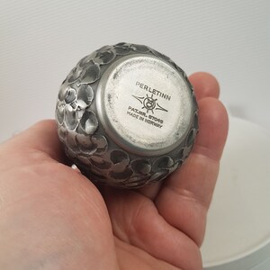 K&ouml;nnte beinhalten: Ein rundes, dekoratives Objekt aus Silber mit einem floralen Design. Die Unterseite des Objekts tr&auml;gt den Text "PERLETINN" und "PAT.NR. 57049 MADE IN NORWAY".