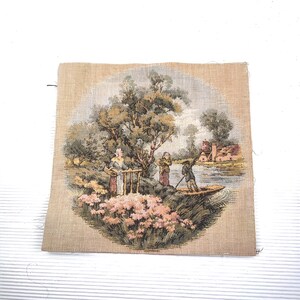 Puede incluir: Un tapiz que representa una escena pastoral con figuras cerca de un río y un edificio al fondo. La obra de arte presenta un barco, árboles y flores rosas, todo sobre un fondo beige.