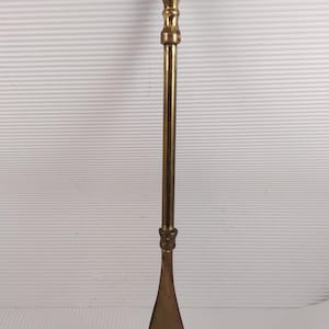 May include: A vintage brass shoe horn with a long handle and a curved, spoon-like end. The handle has a decorative design and a ring at the top. The brass has a warm, aged patina.
