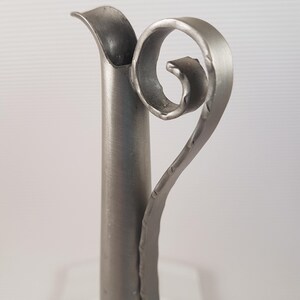K&ouml;nnte beinhalten: Eine silberne Metallvase mit einem einzigartigen, gedrehten Griff. Die Vase hat eine glatte, polierte Oberfl&auml;che und eine zylindrische Form.
