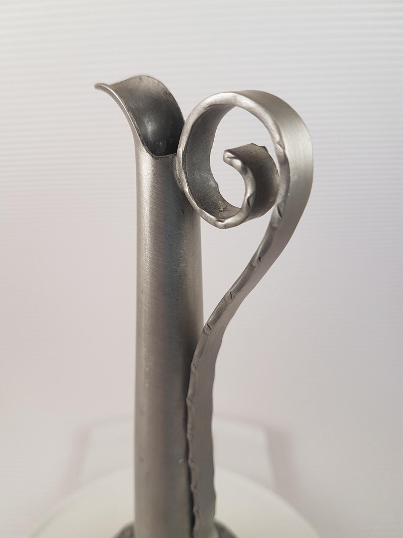 K&ouml;nnte beinhalten: Eine silberne Metallvase mit einem einzigartigen, gedrehten Griff. Die Vase hat eine glatte, polierte Oberfl&auml;che und eine zylindrische Form.