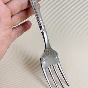 Op de afbeelding: Een zilveren vork met een sierlijk handvat. Het handvat heeft een bloemmotief en is gebogen.